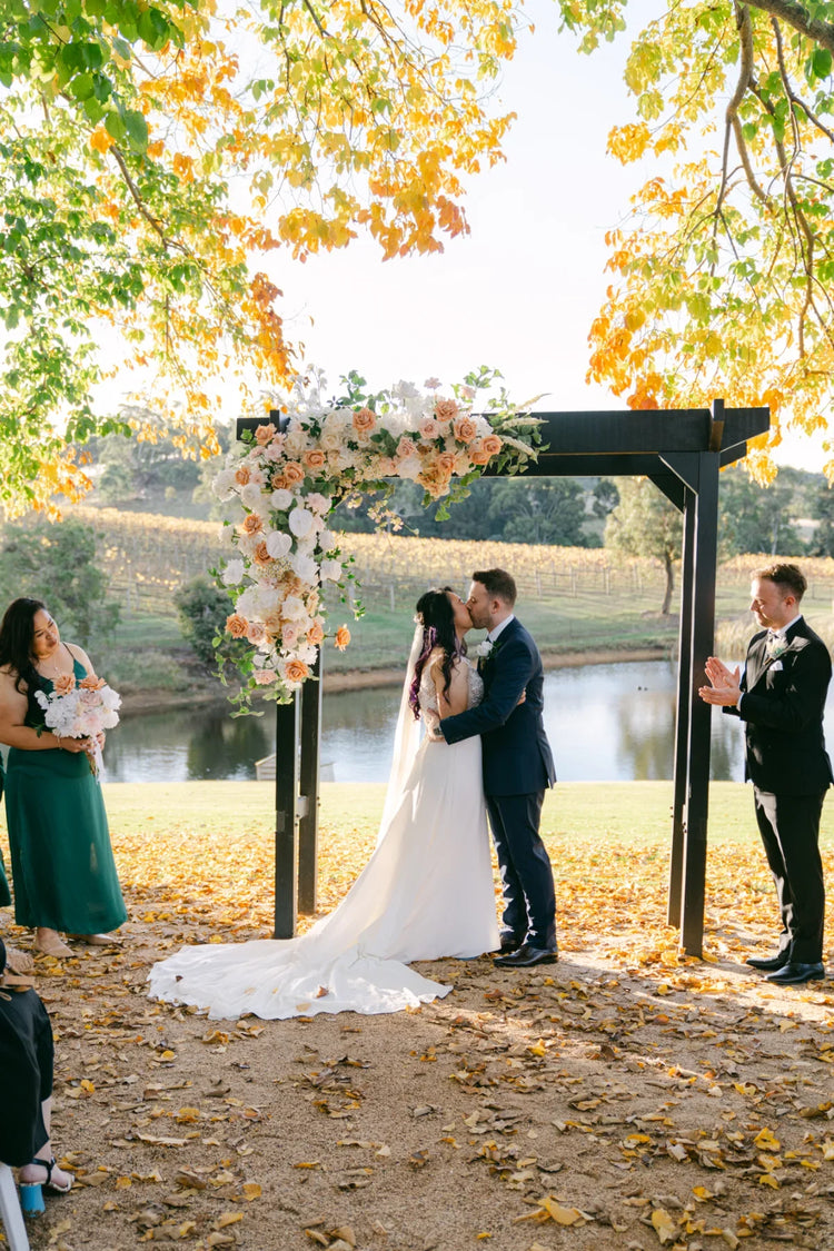 Bride and groom embracing under an arbour with autumn colours in the backgrund