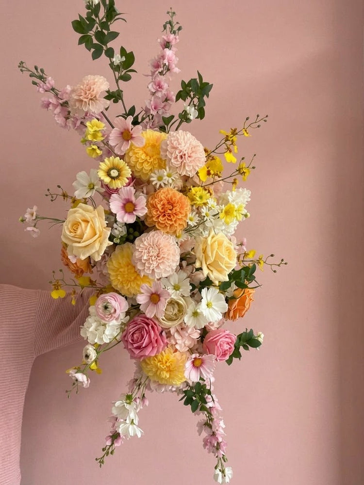 Artificial wedding flowers for arbour held up by a hand with a pink background