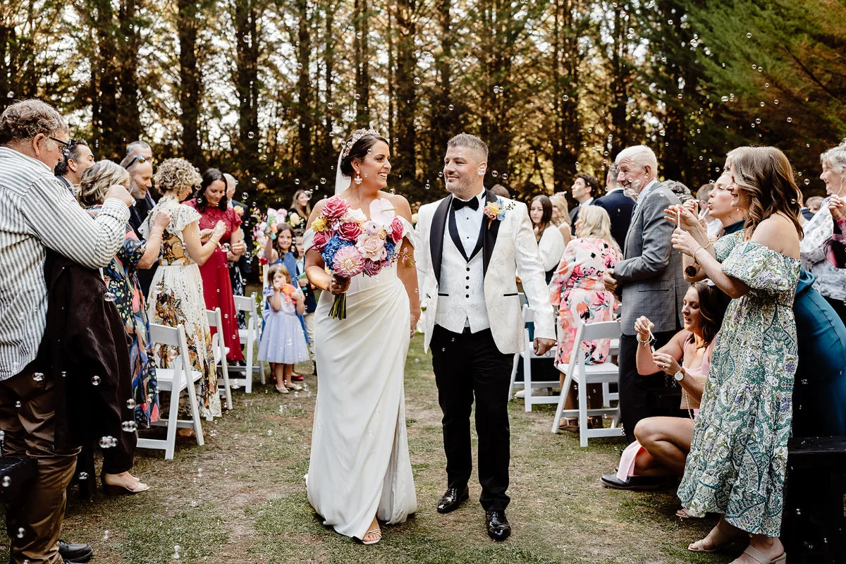 Bride and groom walking down the aisle with guest celebrating in a forest