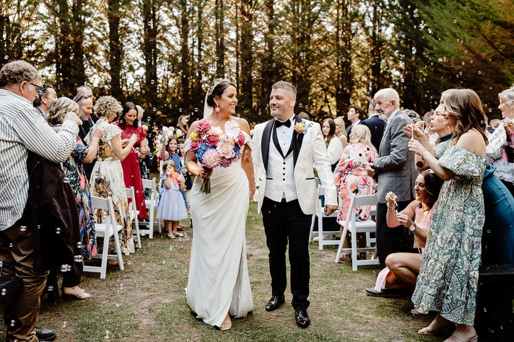 Bride and groom walking down the aisle with guest celebrating in a forest