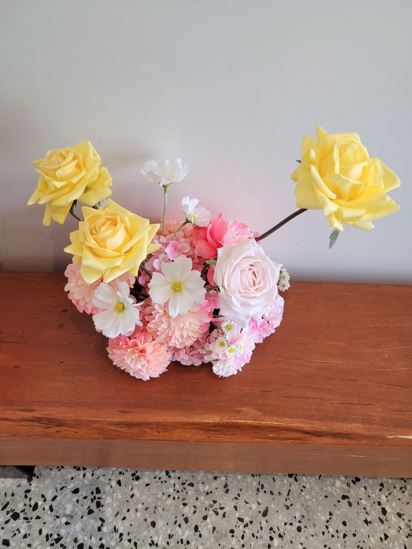 Bouquet of yellow, pink, and white flowers on a wooden surface with a neutral background
