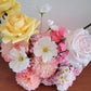 Assorted flowers including yellow, pink, and white on a wooden surface with a light background