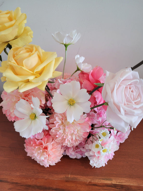 Assorted flowers including yellow, pink, and white on a wooden surface with a light background
