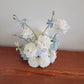 Bouquet of white and light blue flowers on a wooden surface with a neutral background