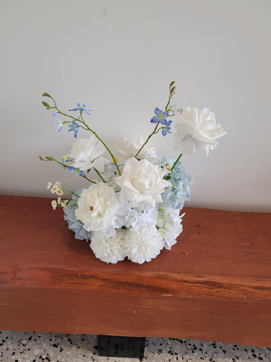 Bouquet of white and light blue flowers on a wooden surface with a neutral background