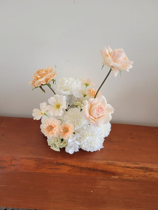 Floral arrangement with peach and white flowers on a wooden surface