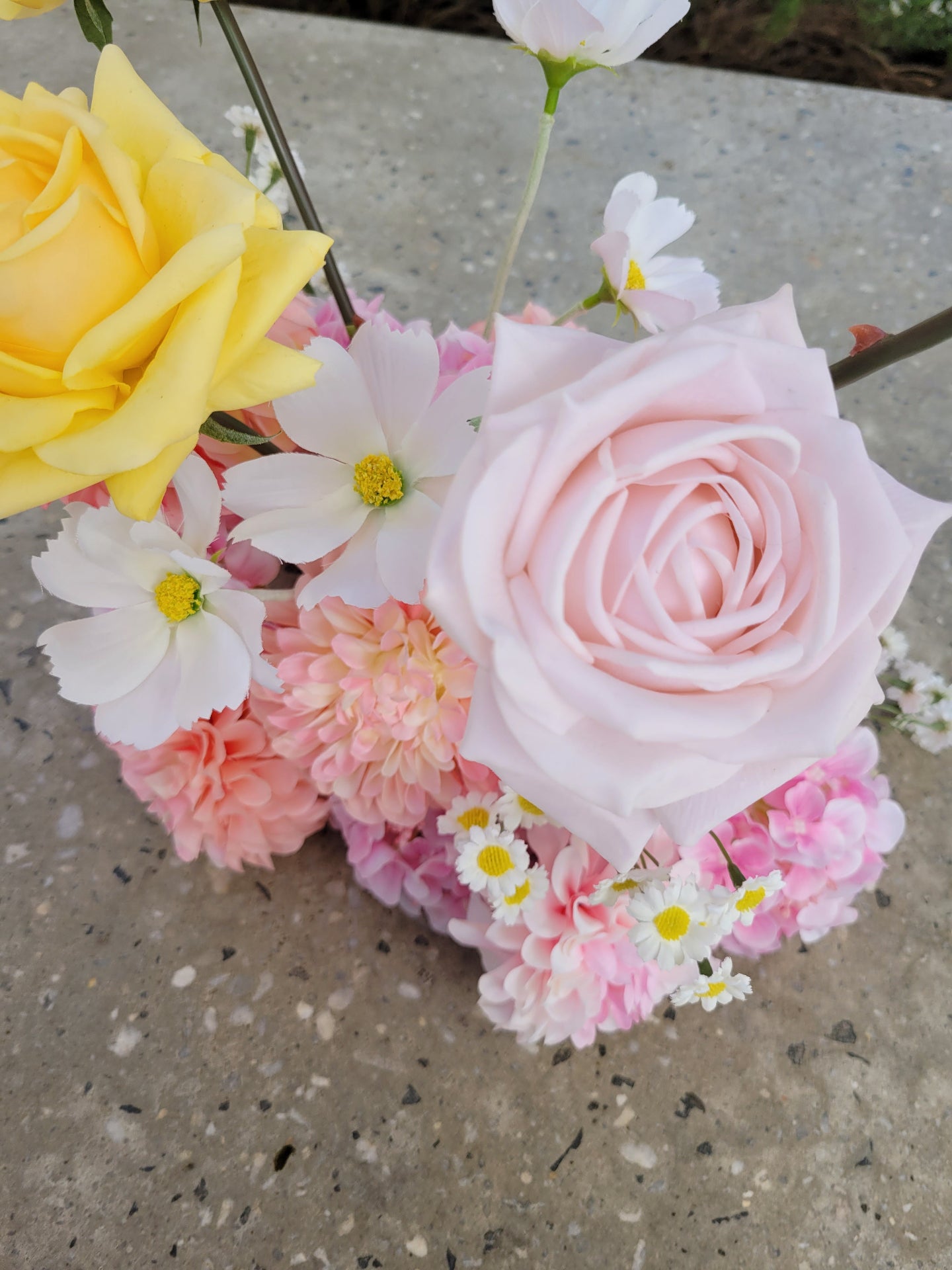 Bouquet of flowers including pink roses, yellow rose, and other assorted flowers on a concrete surface.