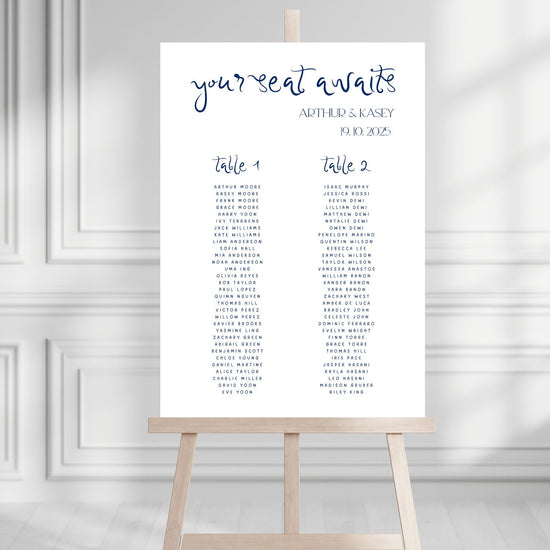 Seating chart poster for a wedding on a wooden stand against a white wall.