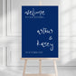 Wedding welcome sign on an easel with a blue background and white text.