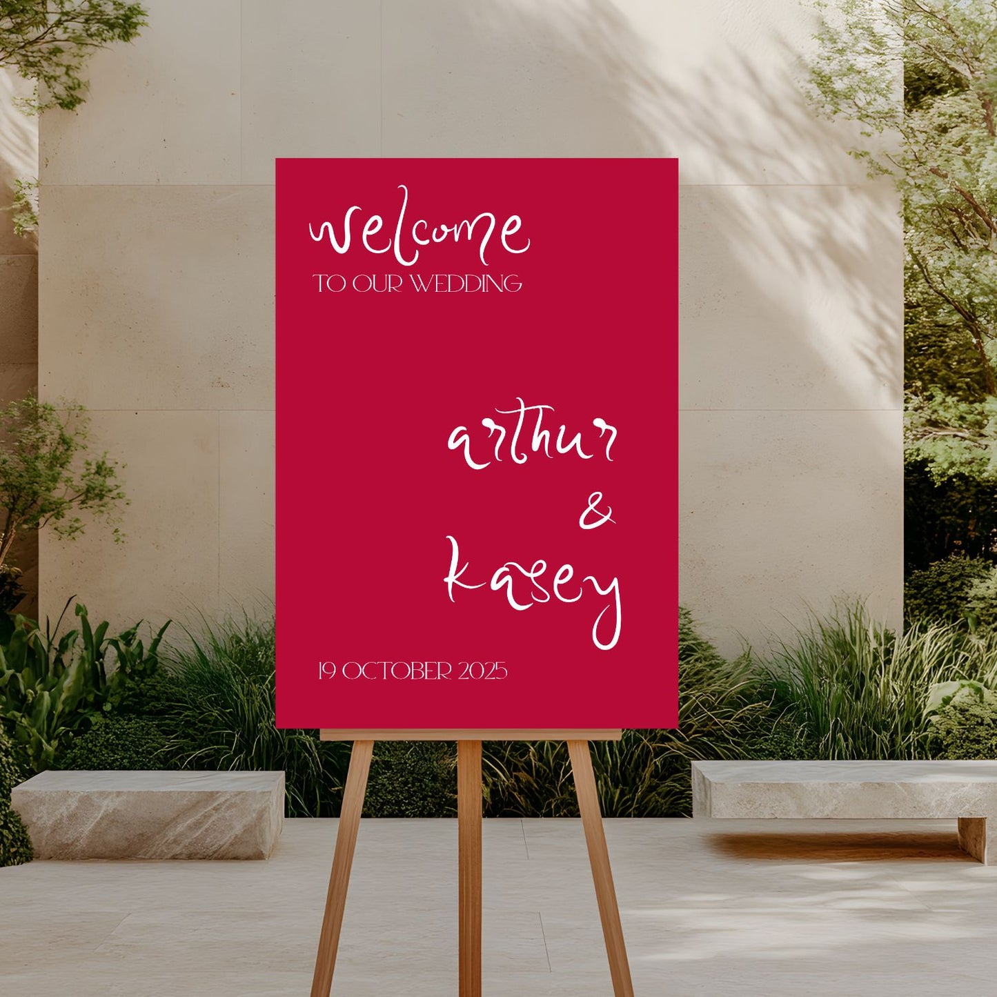 Wedding welcome sign on an easel outdoors with a red background and white text.