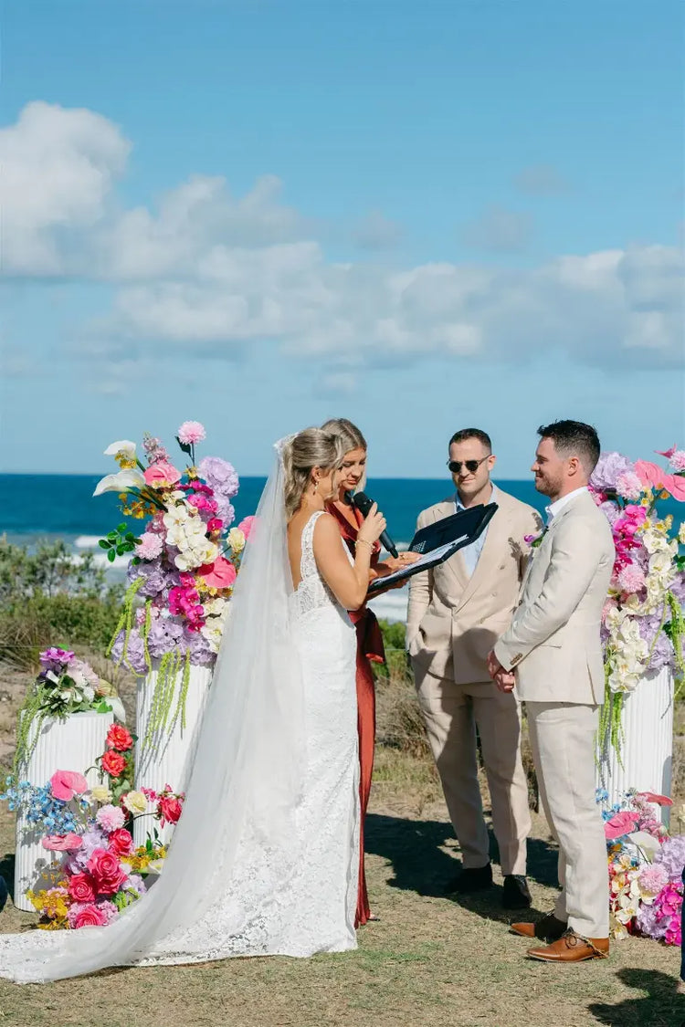 wedding ceremony in front of the ocean with floral arrangements on plinths