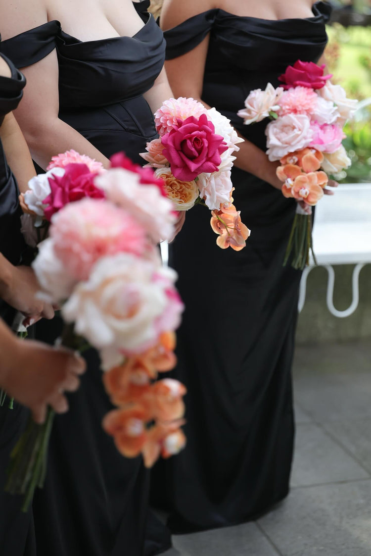 Bridesmaids in black dresses holding floral bouquets with pink, white, and orange flowers.