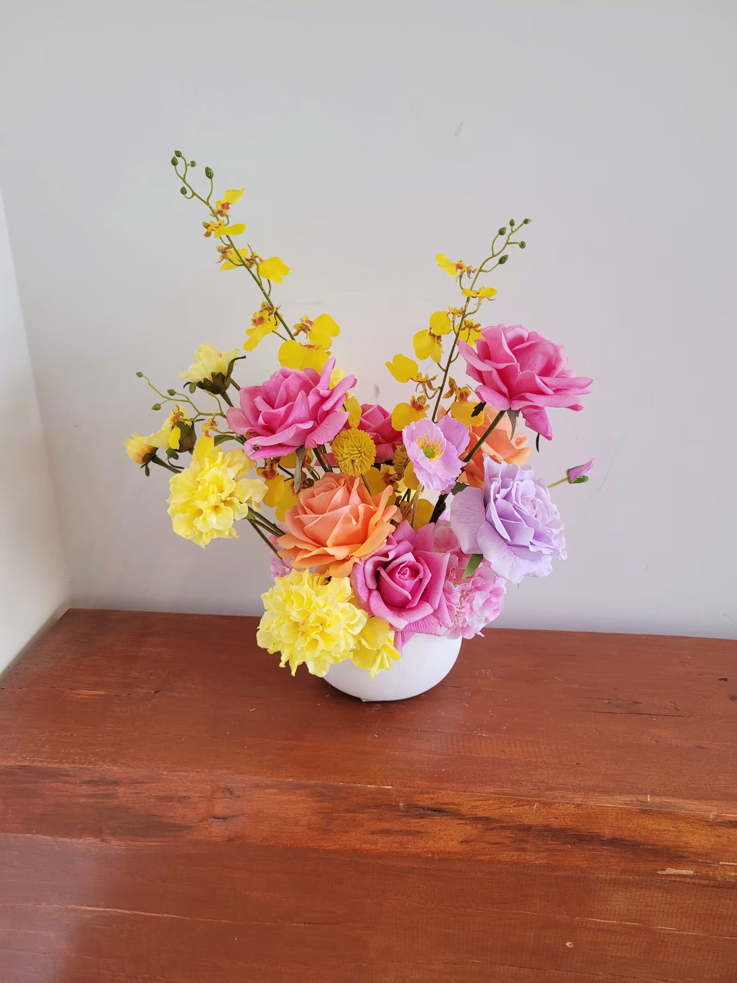 Colorful flower arrangement in a white vase on a wooden surface with a white wall background