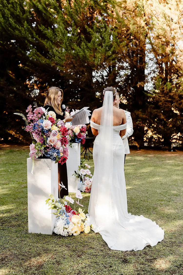 Wedding ceremony showing brides dress and bright wedding flowers on plinths