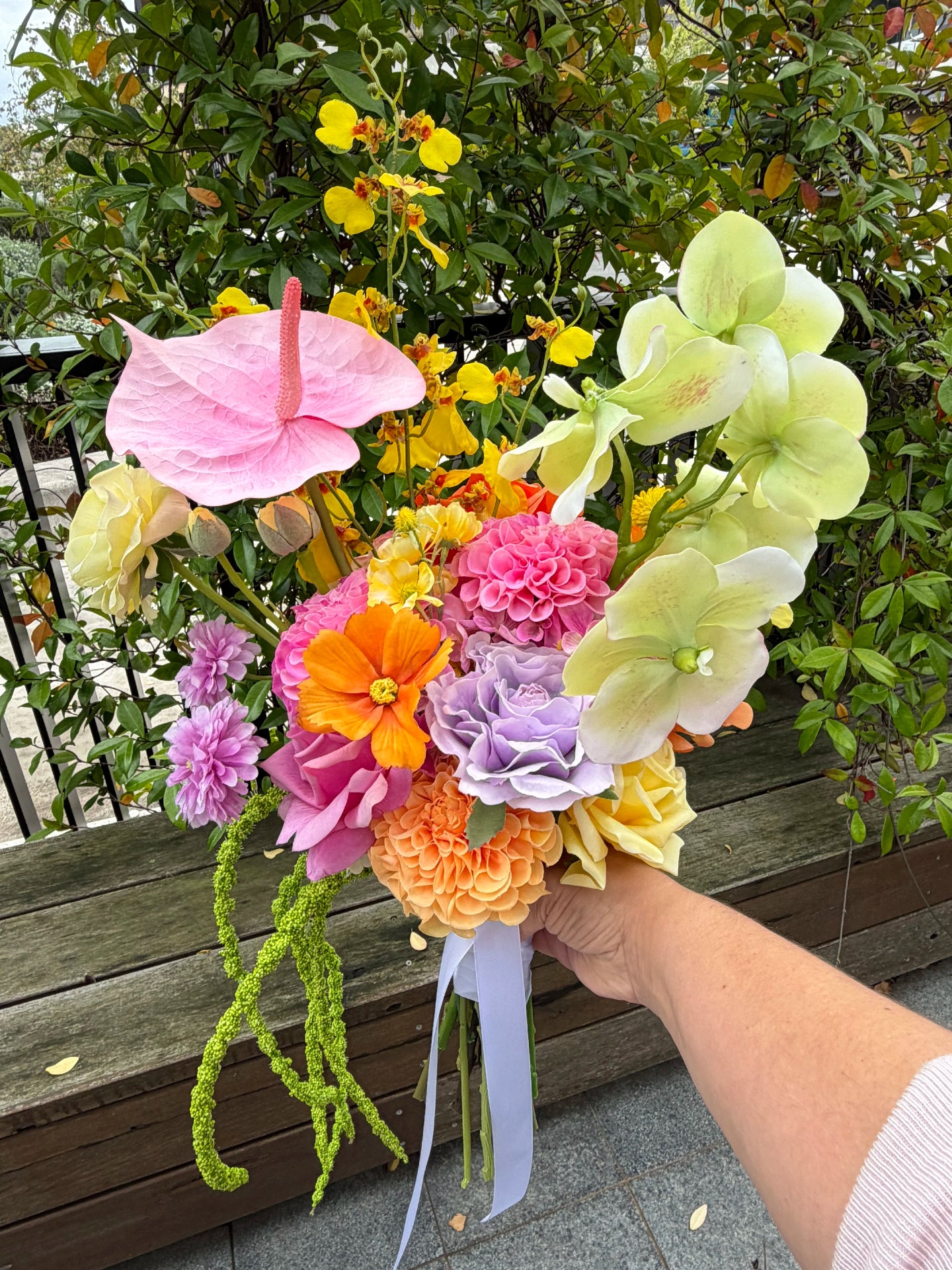 Bouquet of colorful flowers held by a person with greenery in the background