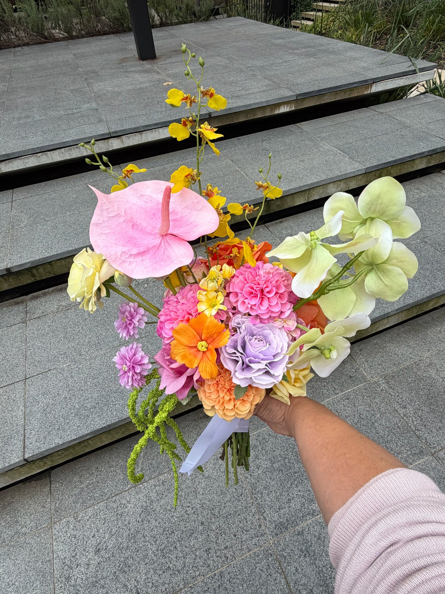 Bouquet of colorful flowers held by a person on a stone pavement.