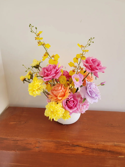 Colourful flower arrangement in a white vase on a wooden surface with a plain background