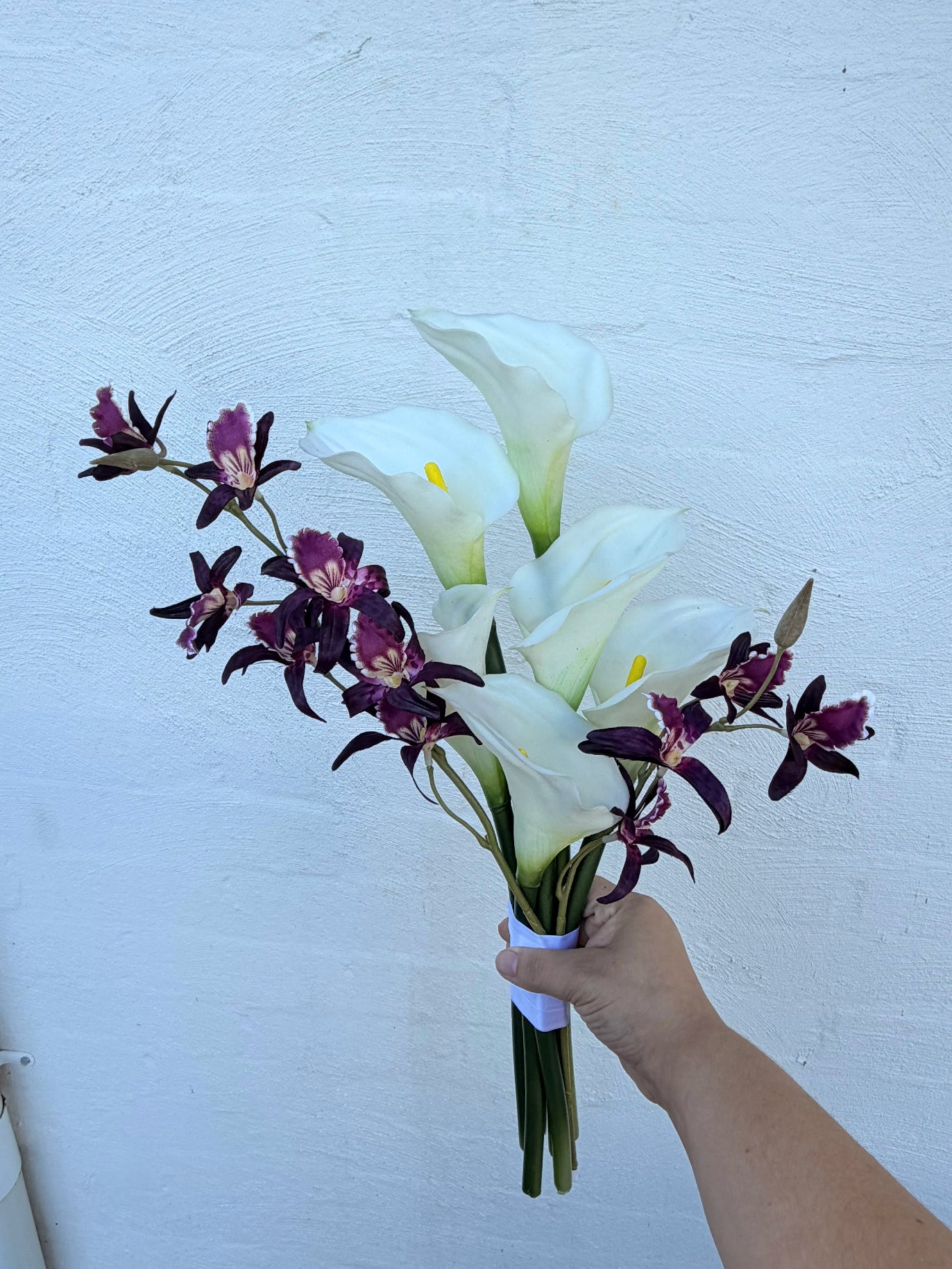 Modern wedding bouquet of white calla lilies with burgundy dendrobium against a white brick wall