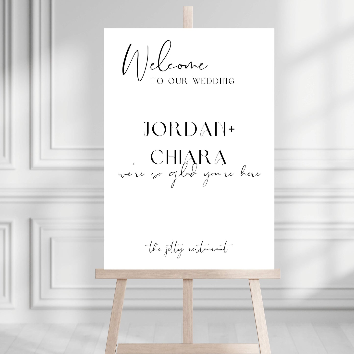 Wedding welcome sign on a wooden stand against a gray wall.