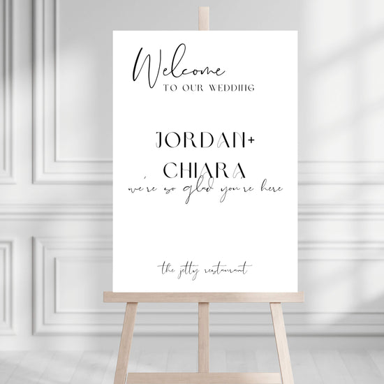 Wedding welcome sign on a wooden stand against a gray wall.