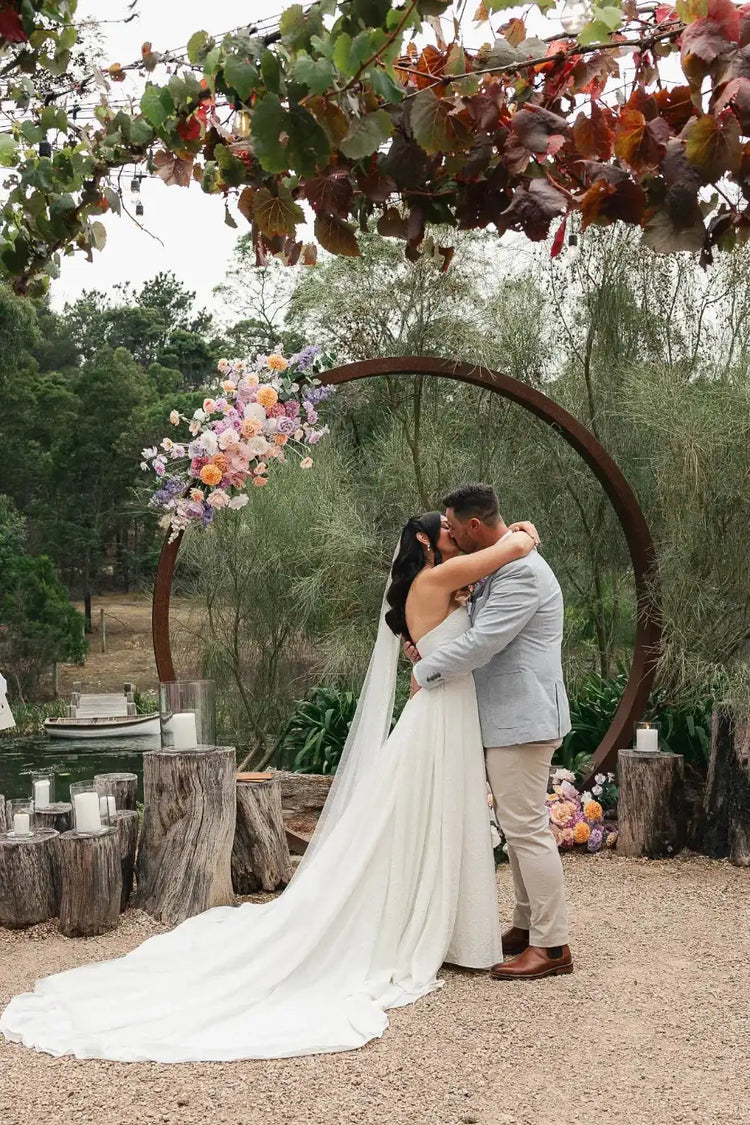 Bride and groom embracing in front of a circular arbour adorned with floral arrangements