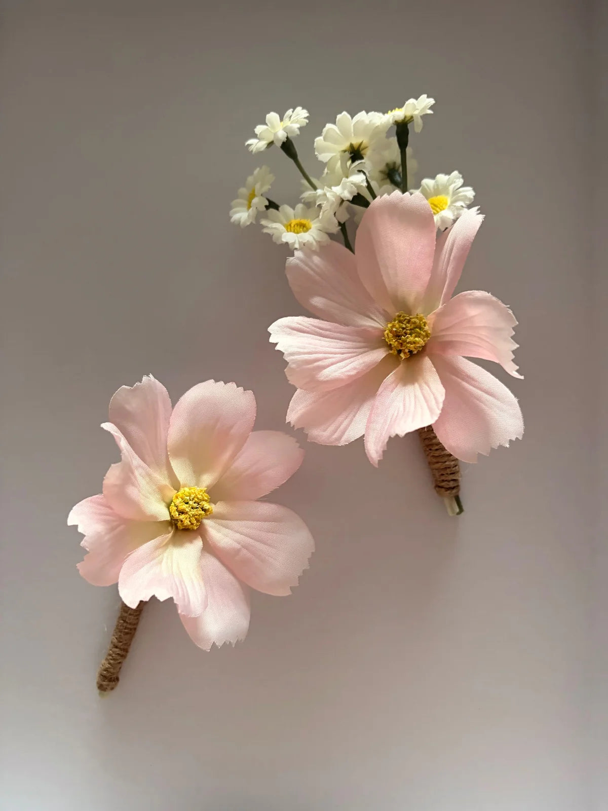 Two pink artificial flowers with yellow centers on a plain background