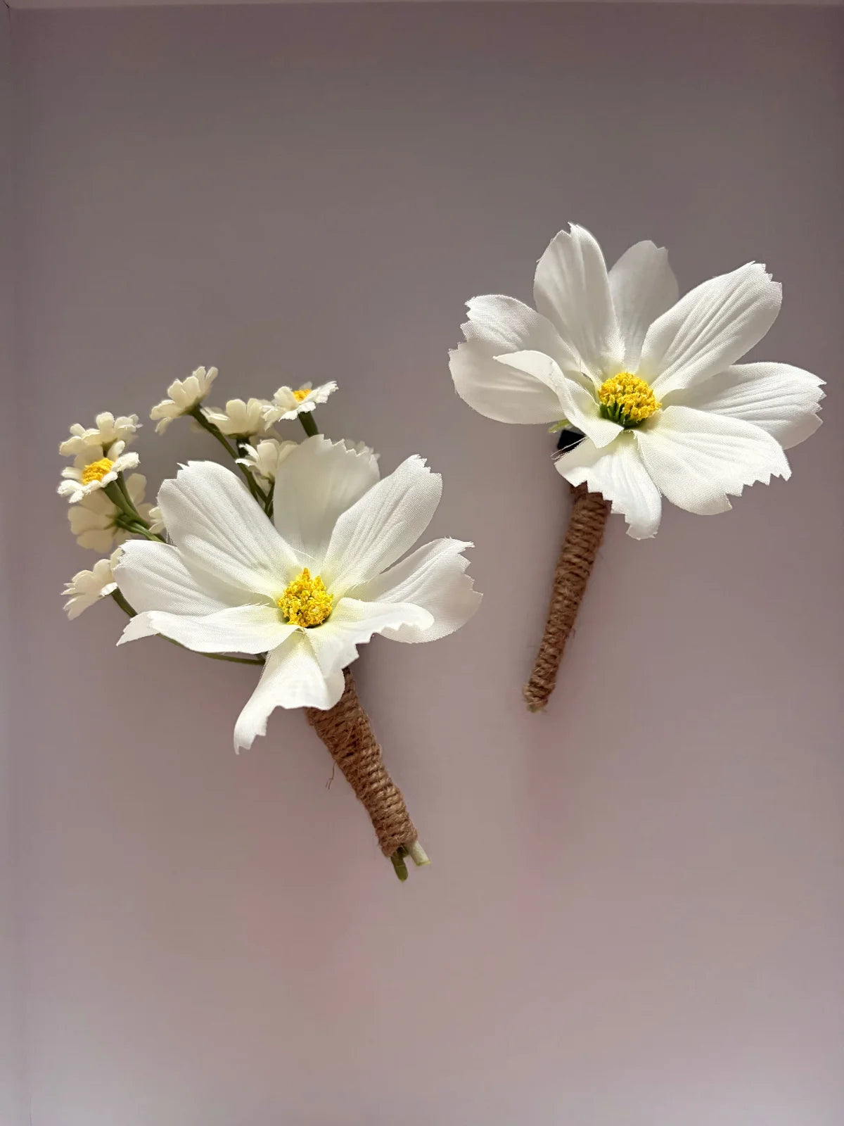 Two white floral boutonnieres with yellow centers on a light gray background