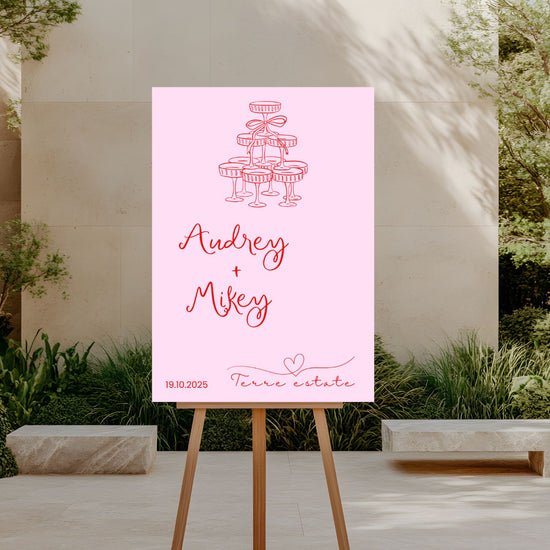Pink poster with 'Audrey + Mikey' and event details on an easel outdoors.