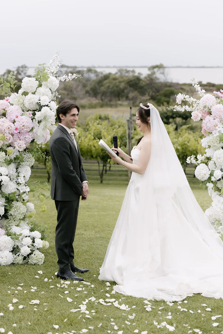 Bride and groom smiling while saying vows in front of large floral towers with hydrangea