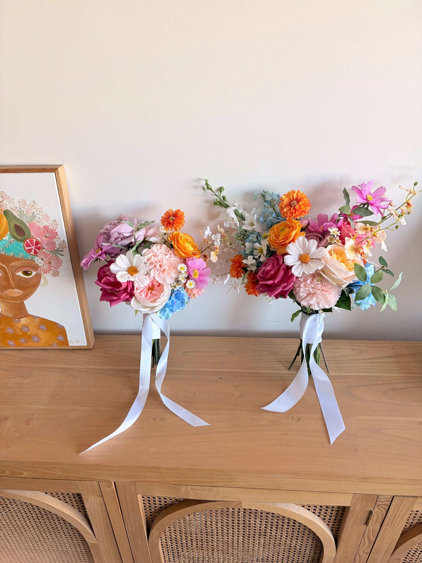 Two colourful artificial wedding bouquets that are different sizes leaning against a wall