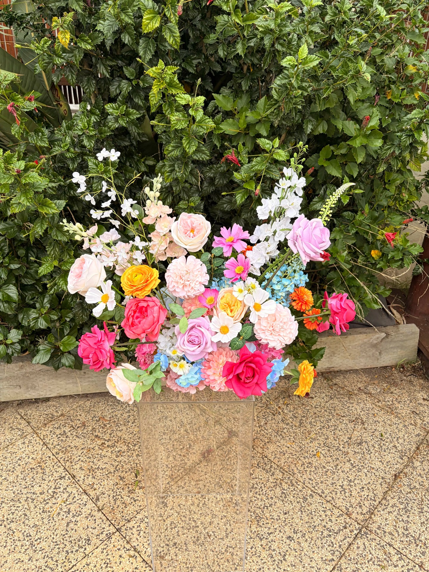 Colorful wedding flower arrangement in a heart shape against a green bush background