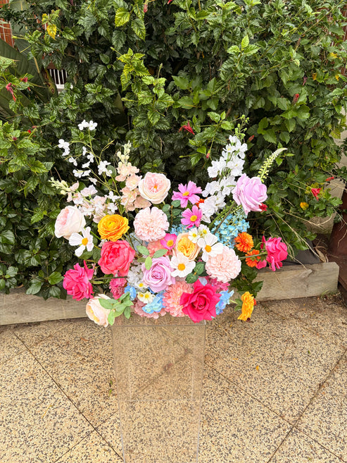 Colorful wedding flower arrangement in a heart shape against a green bush background