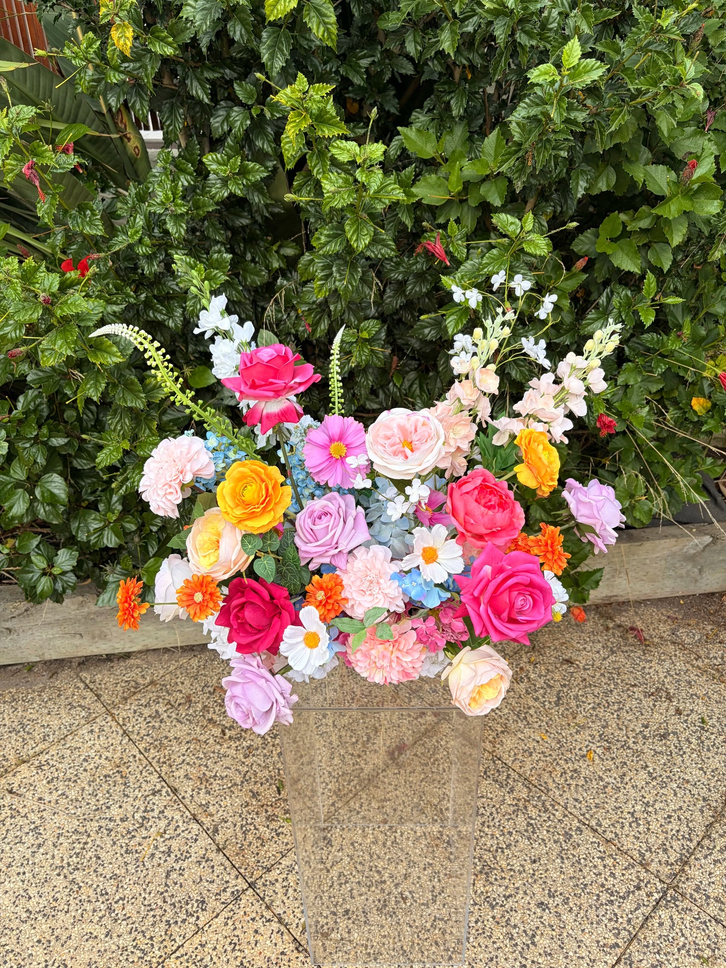 Wedding arrangement of colourful flowers on a clear plinth