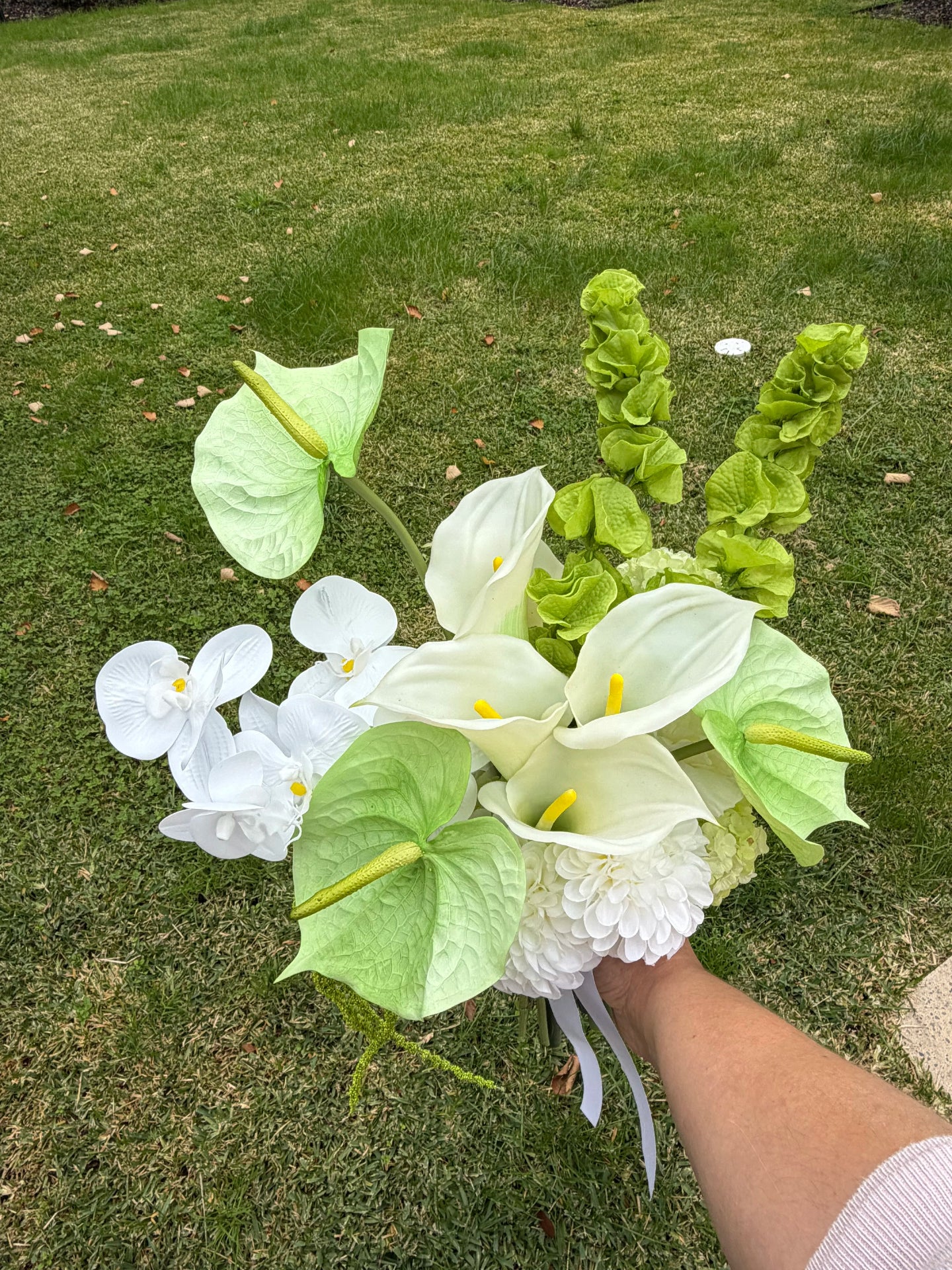 Bouquet of white and green flowers held by a person on grass