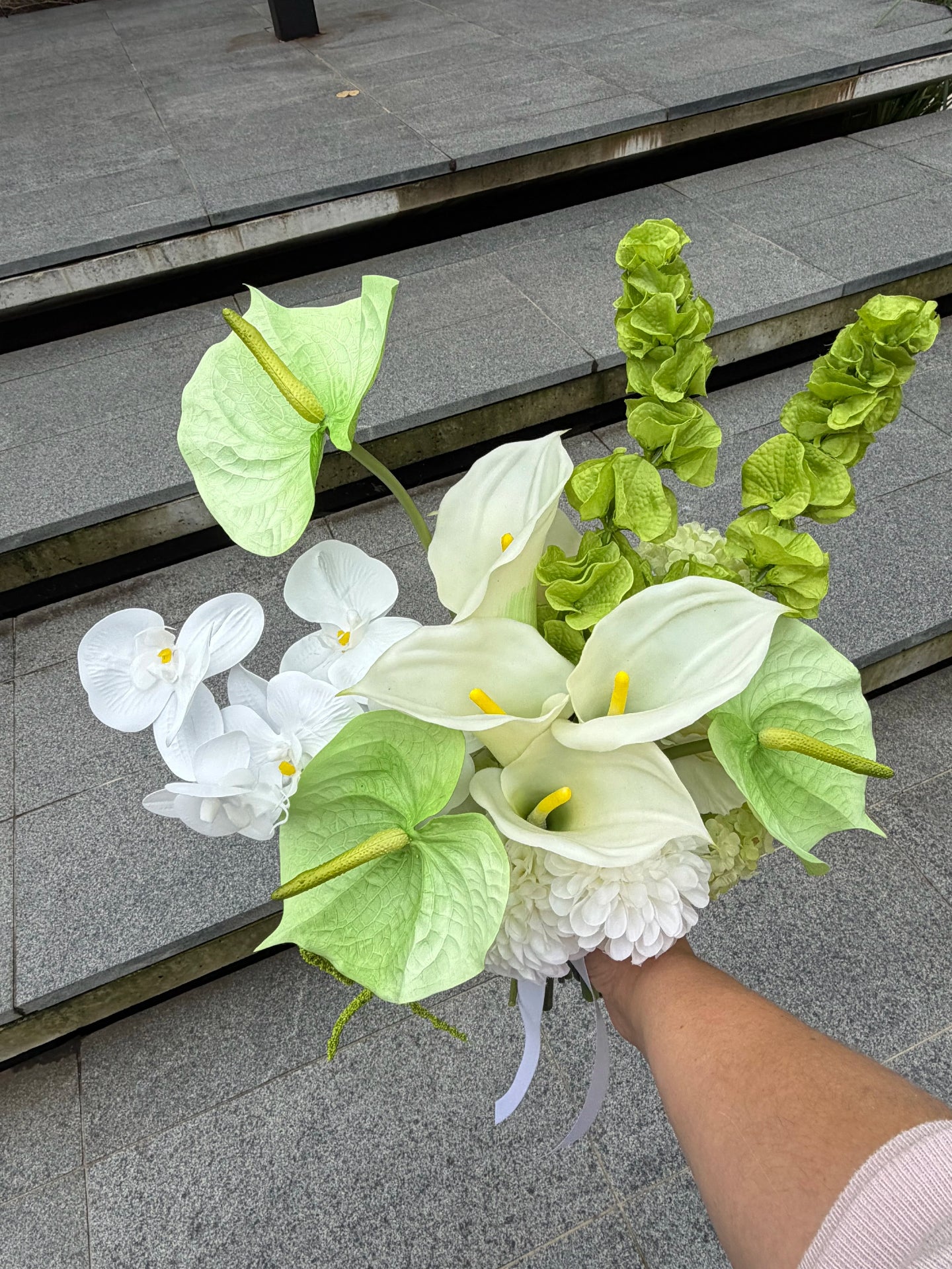 Bouquet of white and green flowers held by a person on stone steps.