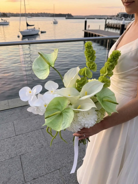 Bouquet of flowers held by a person in a white dress by a waterfront with sailboats.
