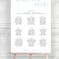 Seating chart for a wedding on a white board with a wooden stand against a gray background