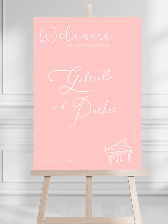Pink welcome sign for a wedding with a piano illustration on a stand against a light gray background.