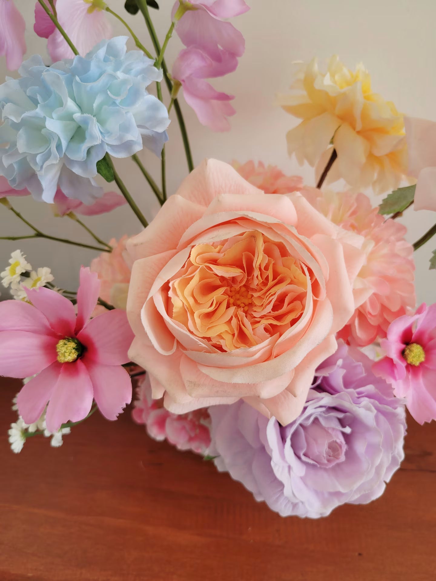 Colorful bouquet of flowers including pink, peach, blue, and purple on a wooden surface.