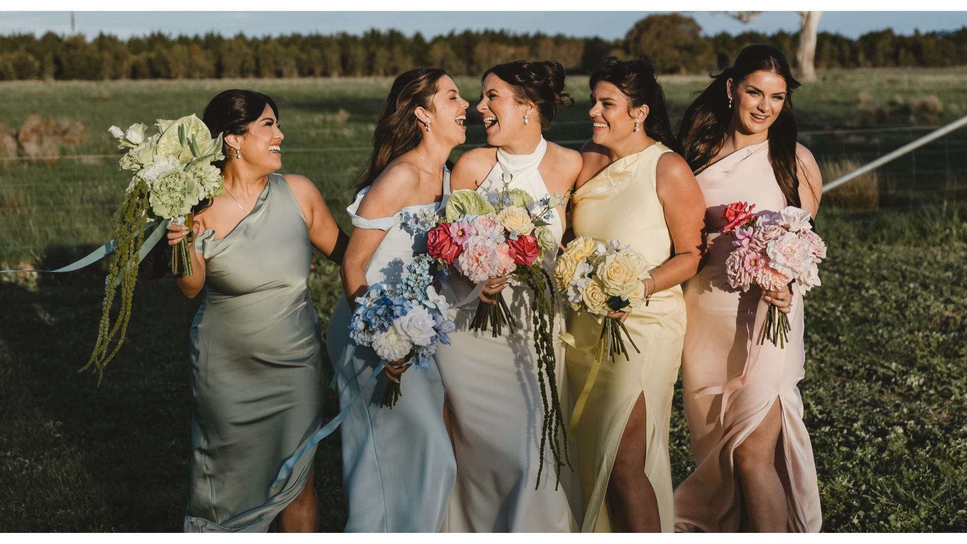 Bride and bridesmaids in formal dresses with artificial floral bouquets standing in a field.