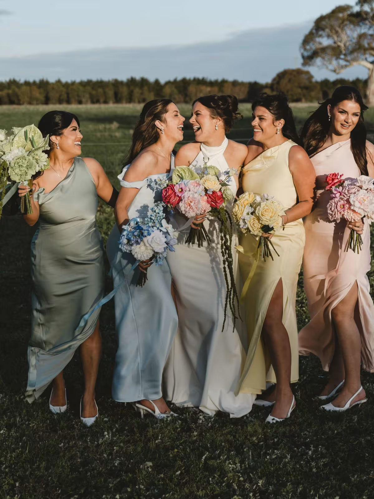 Bridal party in colorful dresses standing outdoors with bouquets.