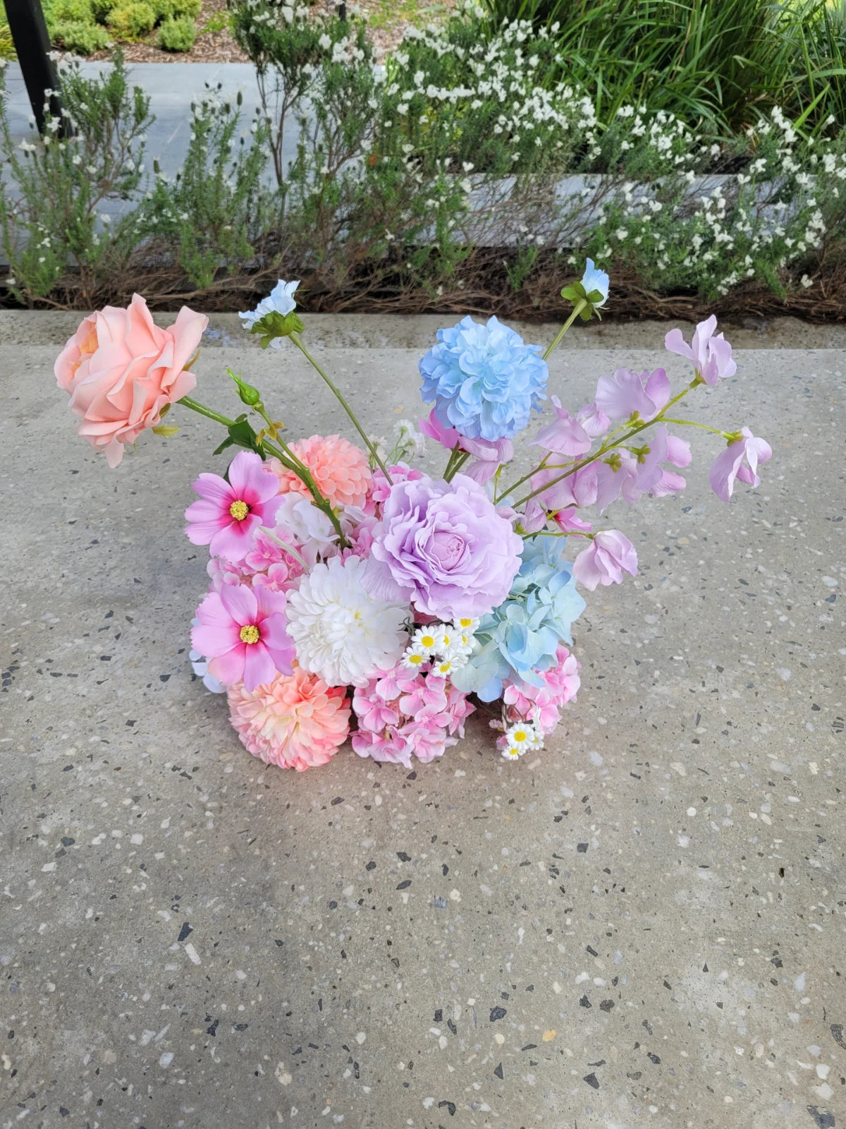 Pastel-coloured flower cloud on a concrete surface with greenery in the background