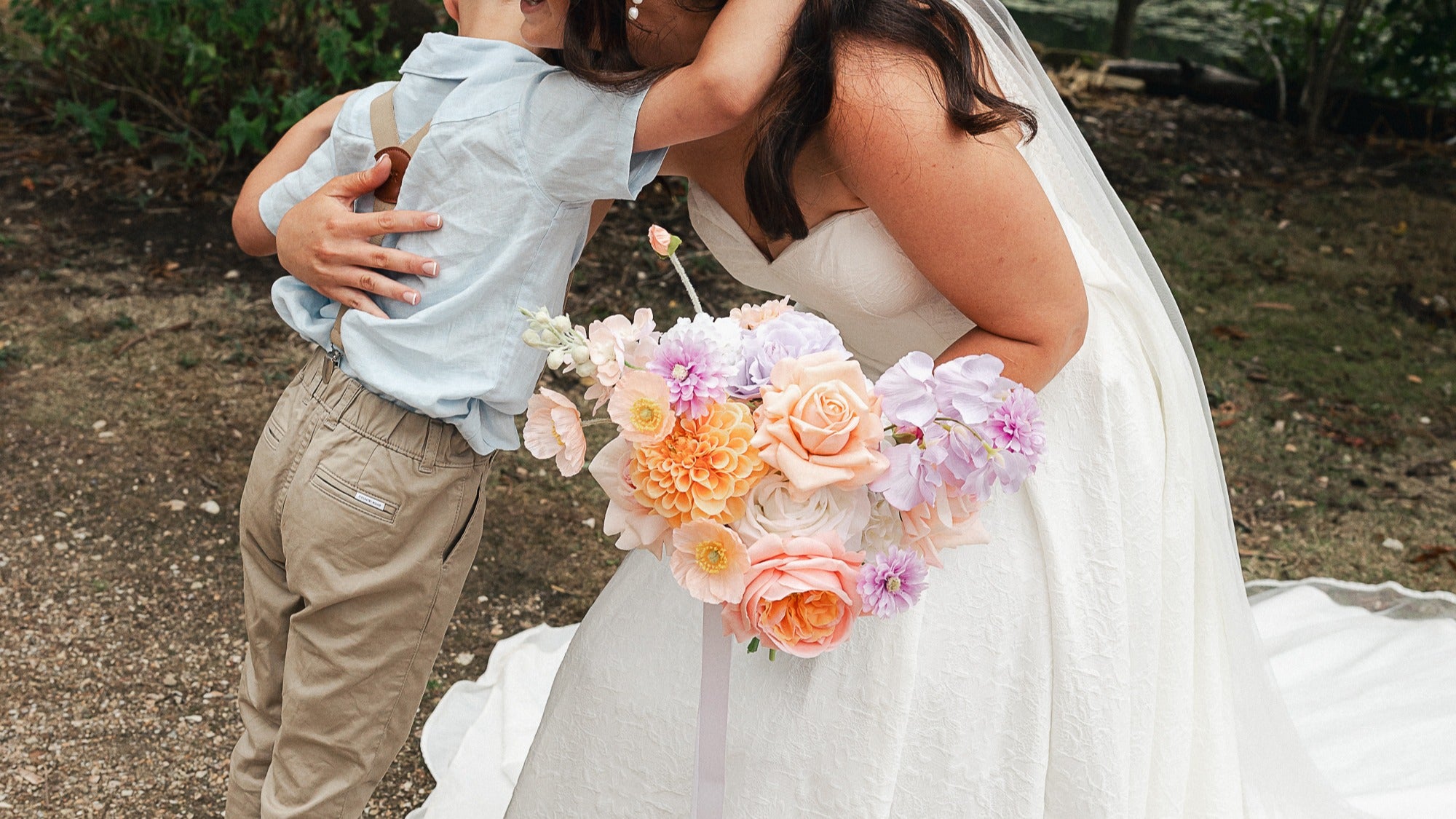 Bride holding a pastel bouquet of flowers while hugging her son