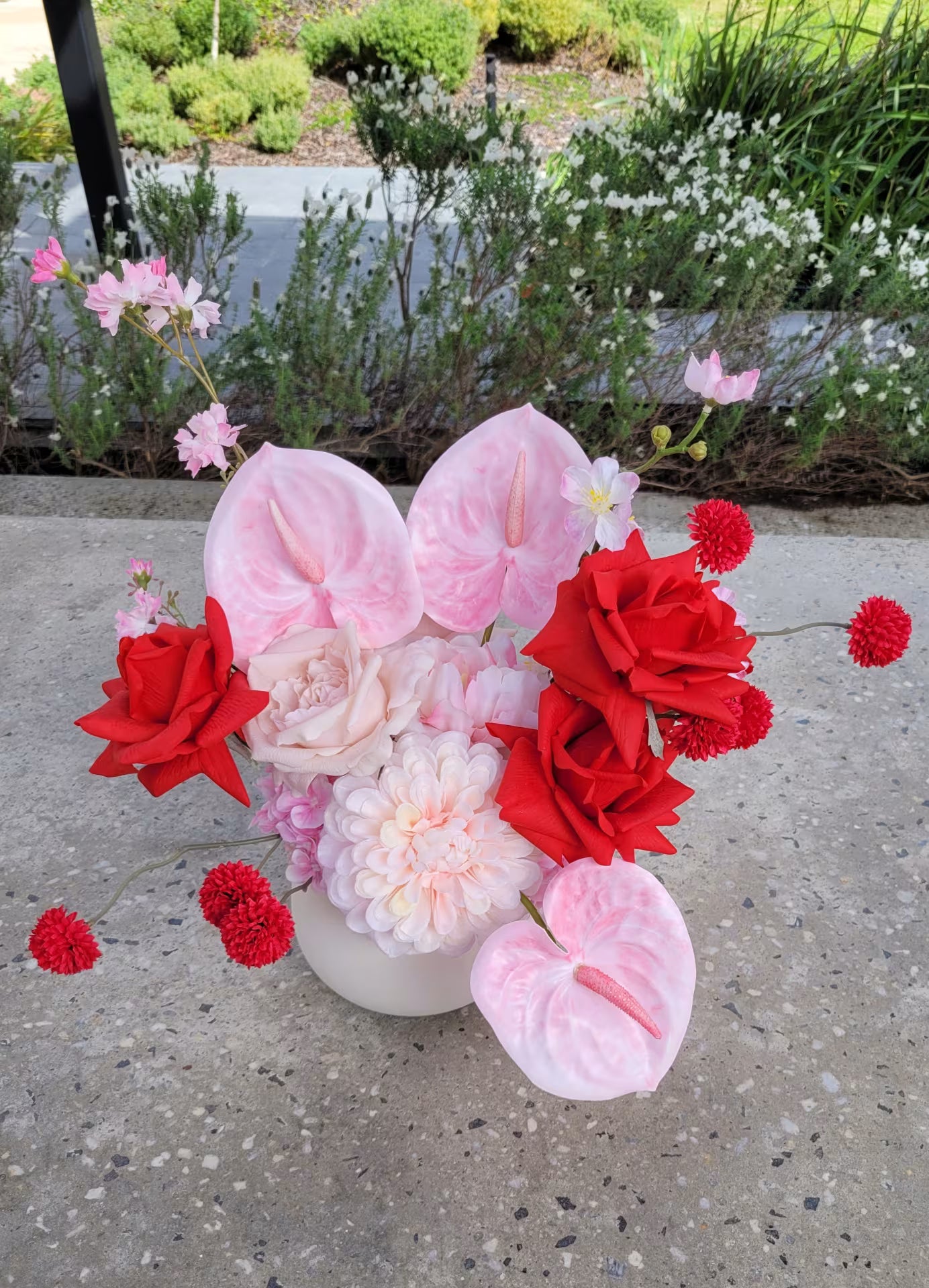 Flower arrangement of red and pink flowers on a concrete bench