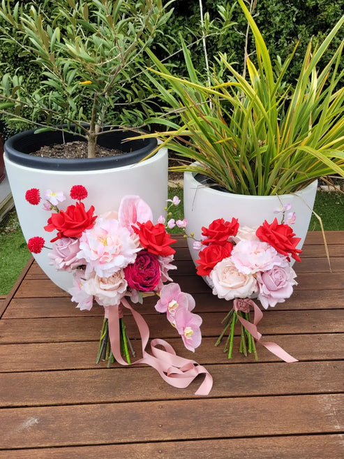 Two flower pots with floral arrangements on a wooden surface outdoors.