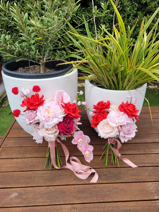 Two flower pots with floral arrangements on a wooden surface outdoors.