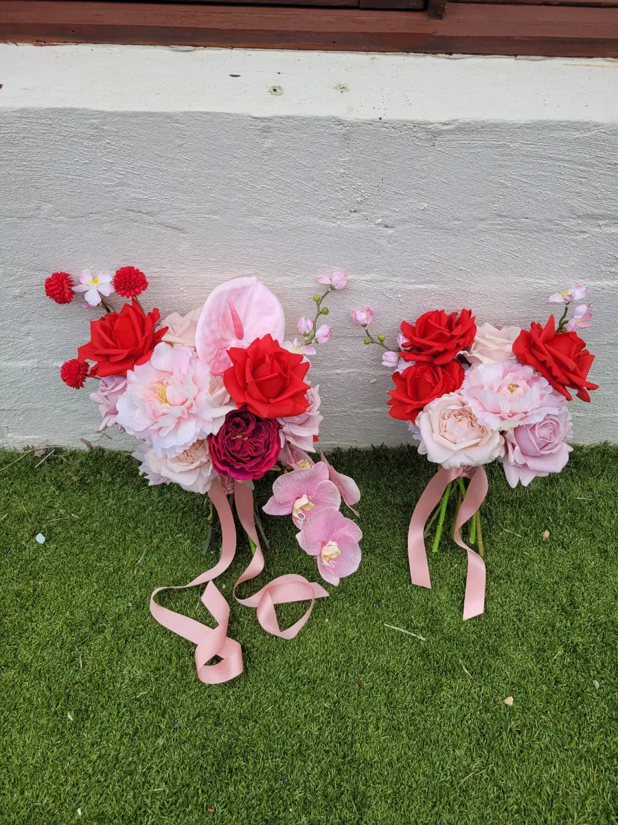 Two artificial wedding bouquets with red and pink flowers on a grassy surface.
