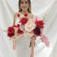 Woman holding two large wedding bouquets of red and pink flowers against a white background