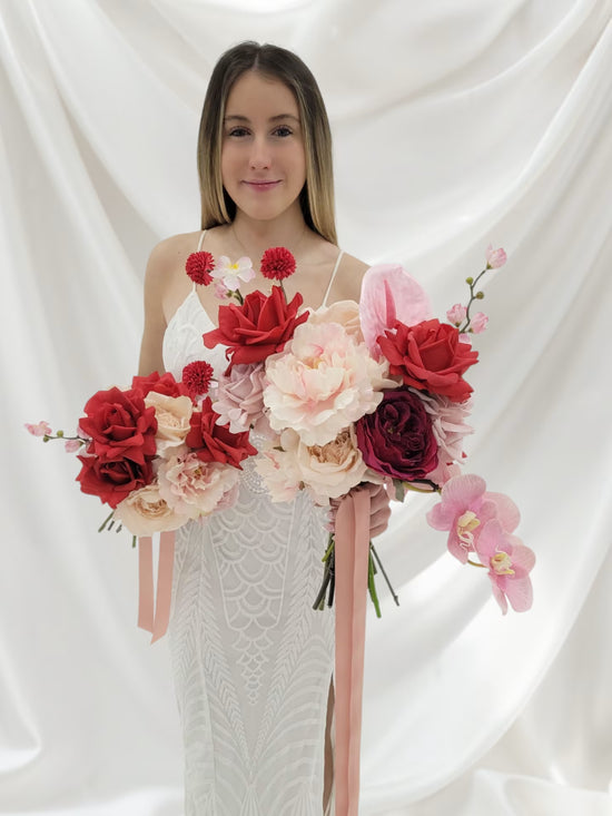 Woman holding two large wedding bouquets of red and pink flowers against a white background