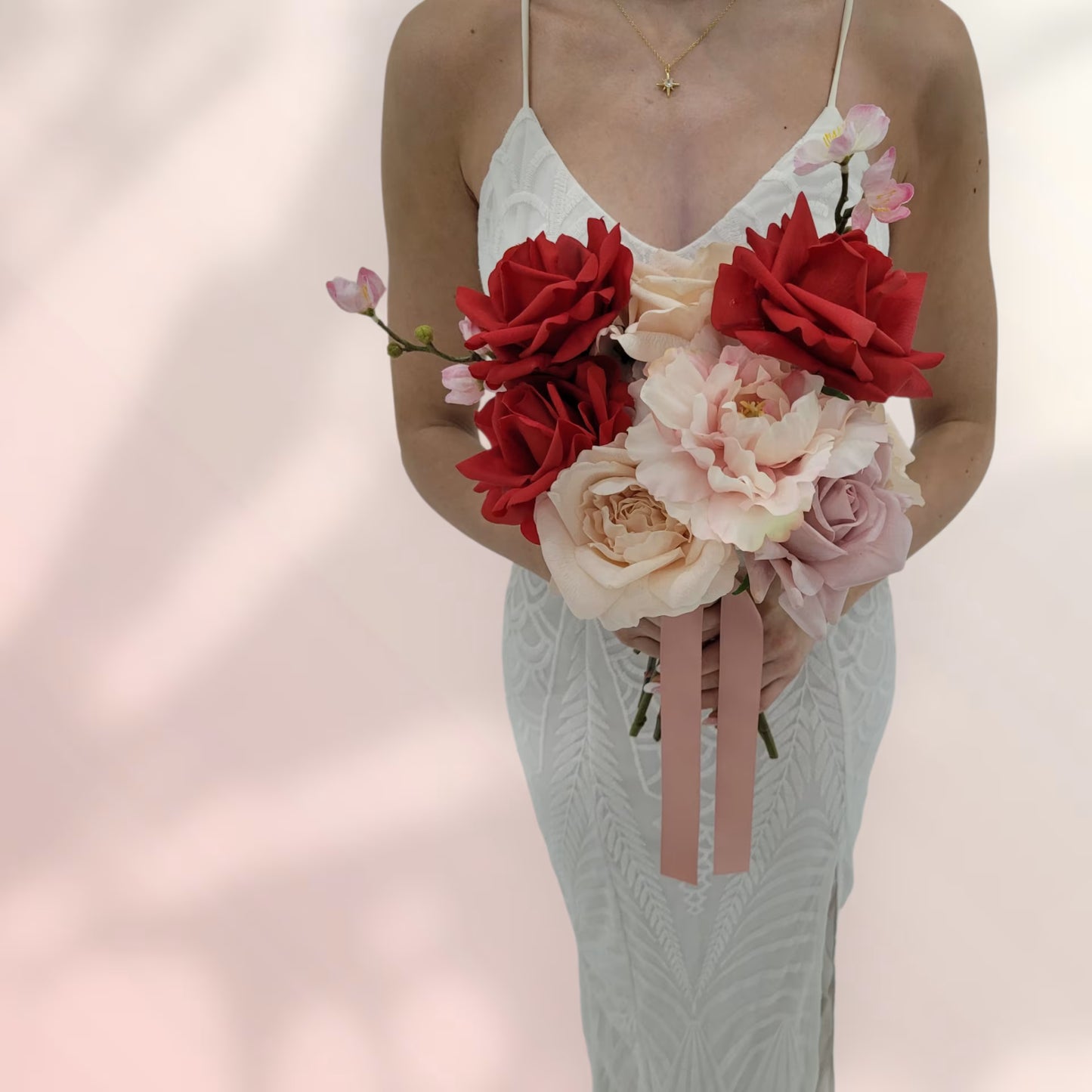 Woman holding a wedding bouquet of red and pink flowers against a soft pink background